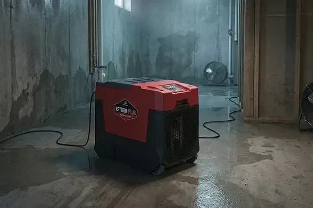 A dehumidifier running on a wet concrete basement floor