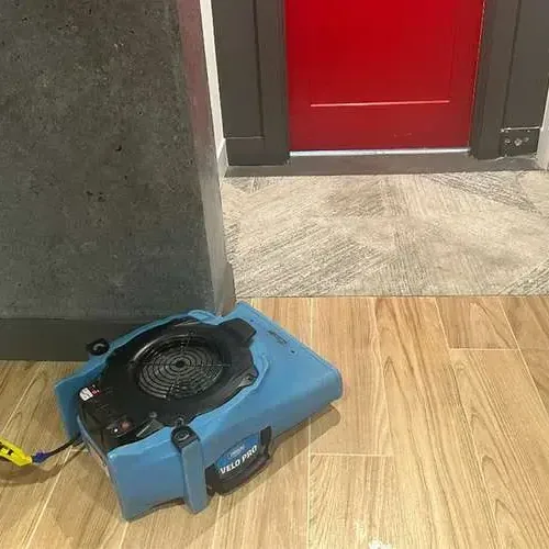 An air mover running on a wood-look tile floor beside an open doorway in a room being dried