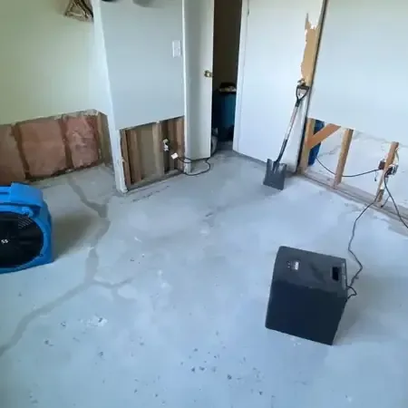 Air movers and a dehumidifier running in a room with the lower drywall cut away and a bare floor