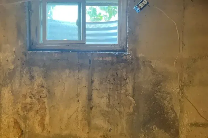 Water stains running down a basement wall under an egress window after the window well filled